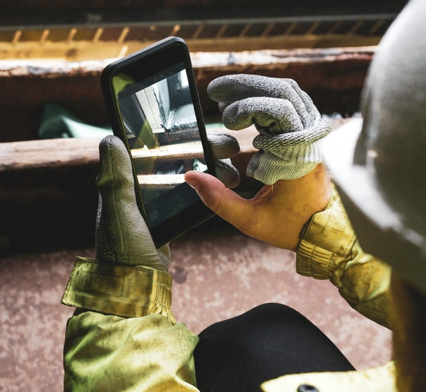Architect holding a smartphone on construction site. young construction worker is using mobile phone on site. Construction worker with building plans and cellphone. Focus on mobile. warm vivid filter. Top view of two construction workers wearing hardhats